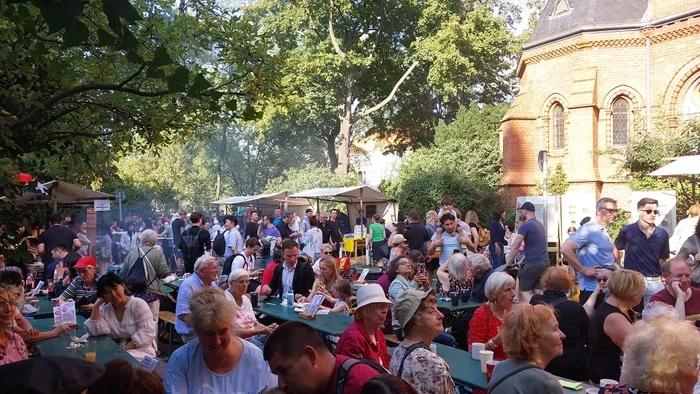 Überfüllte Outdoor-Veranstaltung mit sitzenden Menschen und Kirche im Hintergrund.